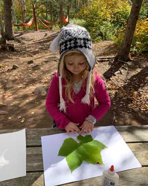 Girl putting a large leaf on a piece of paper