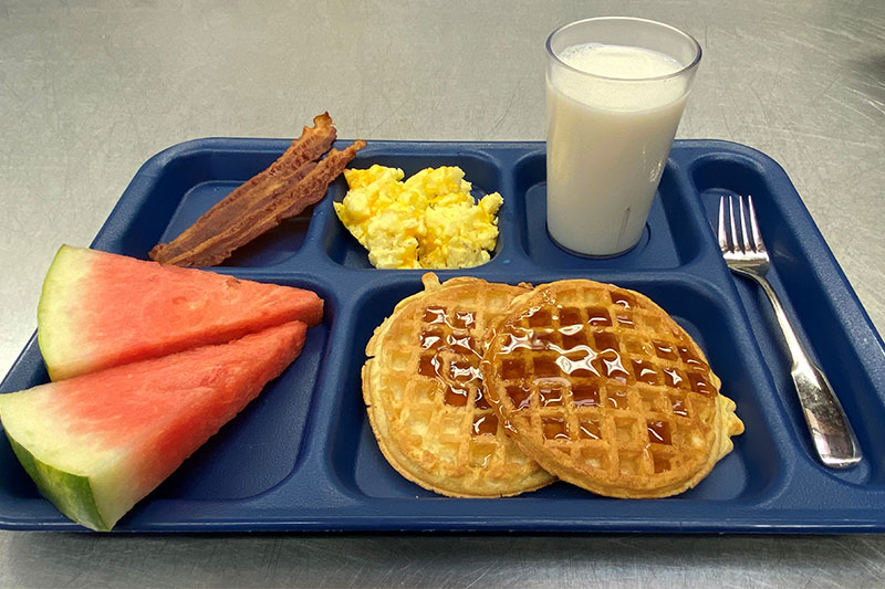 Waffles with eggs, bacon, watermelon, and milk on tray with fork