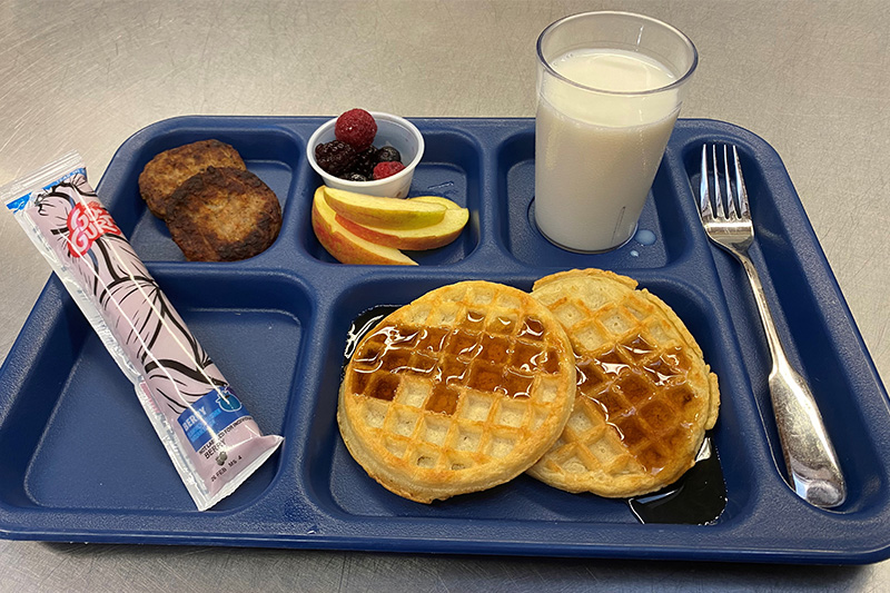 Waffles, sausage patties, yogurt, fruit, milk on tray with fork